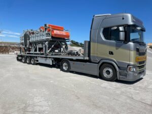 Camión con carga sobredimensionada, transportando maquinaria pesada en cantera.