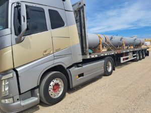 Camión transportando cilindros industriales sobre plataforma, asegurados con correas naranjas